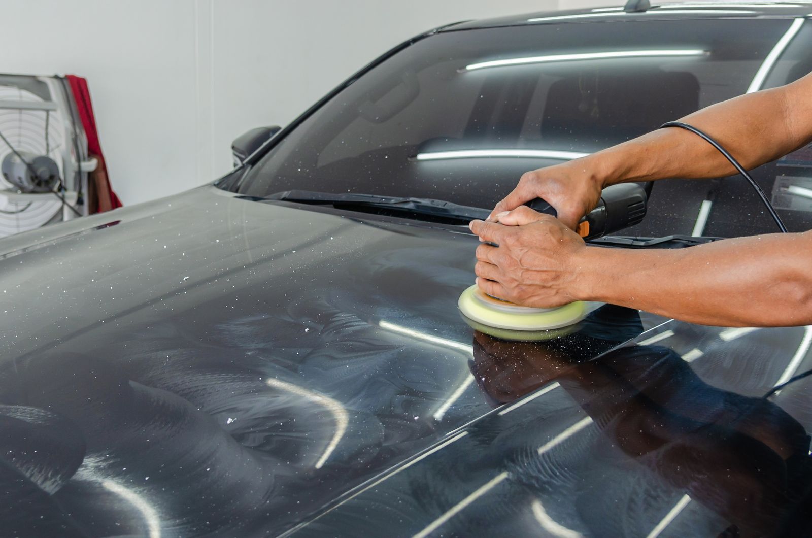 Whole vehicle detailing photograph - mechanic polishing a black car in the workshop