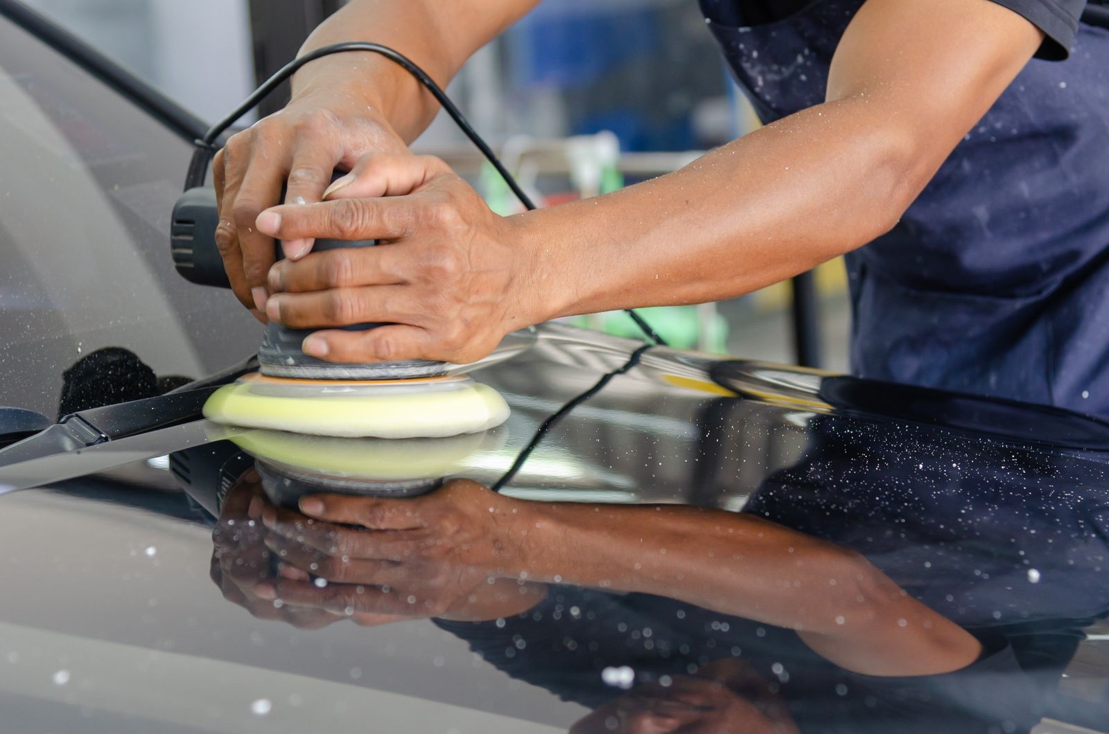 Paint correction photograph - detailer's hands machine polishing a car hood